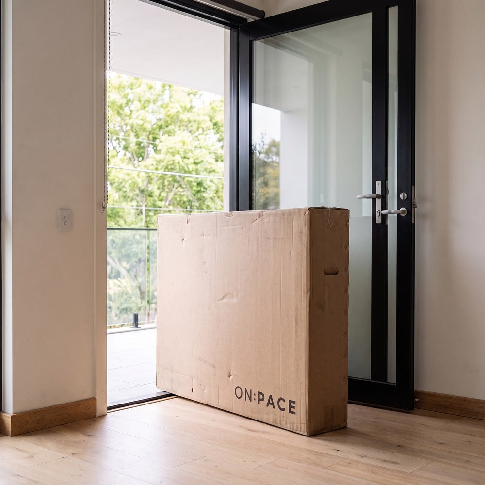 An ON:PACE treadmill carton delivered inside a front door