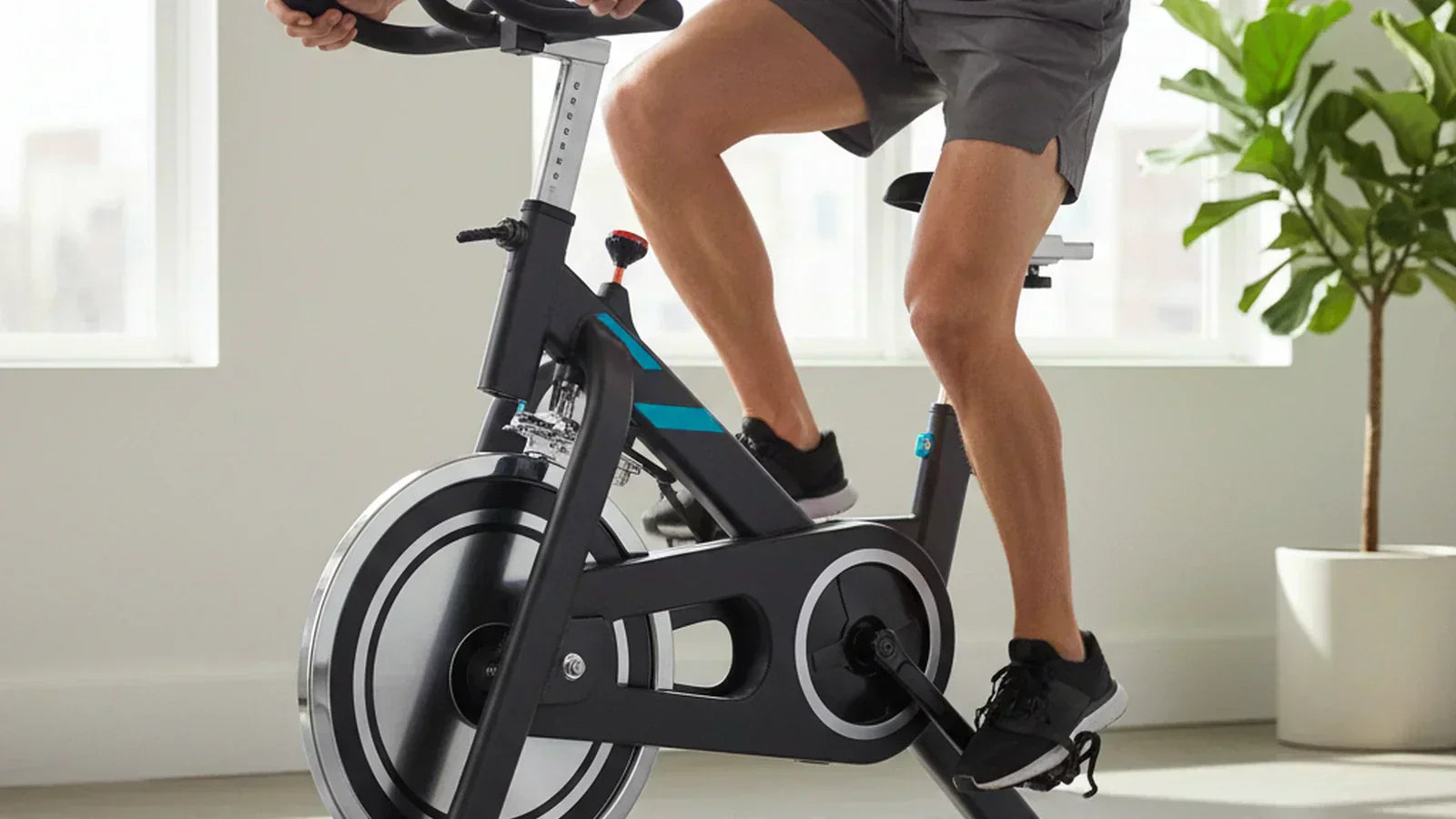 Spin bike in a sunlit Australian home gym with a heavy chrome flywheel, dual-sided pedals and a tablet shelf on the handlebars