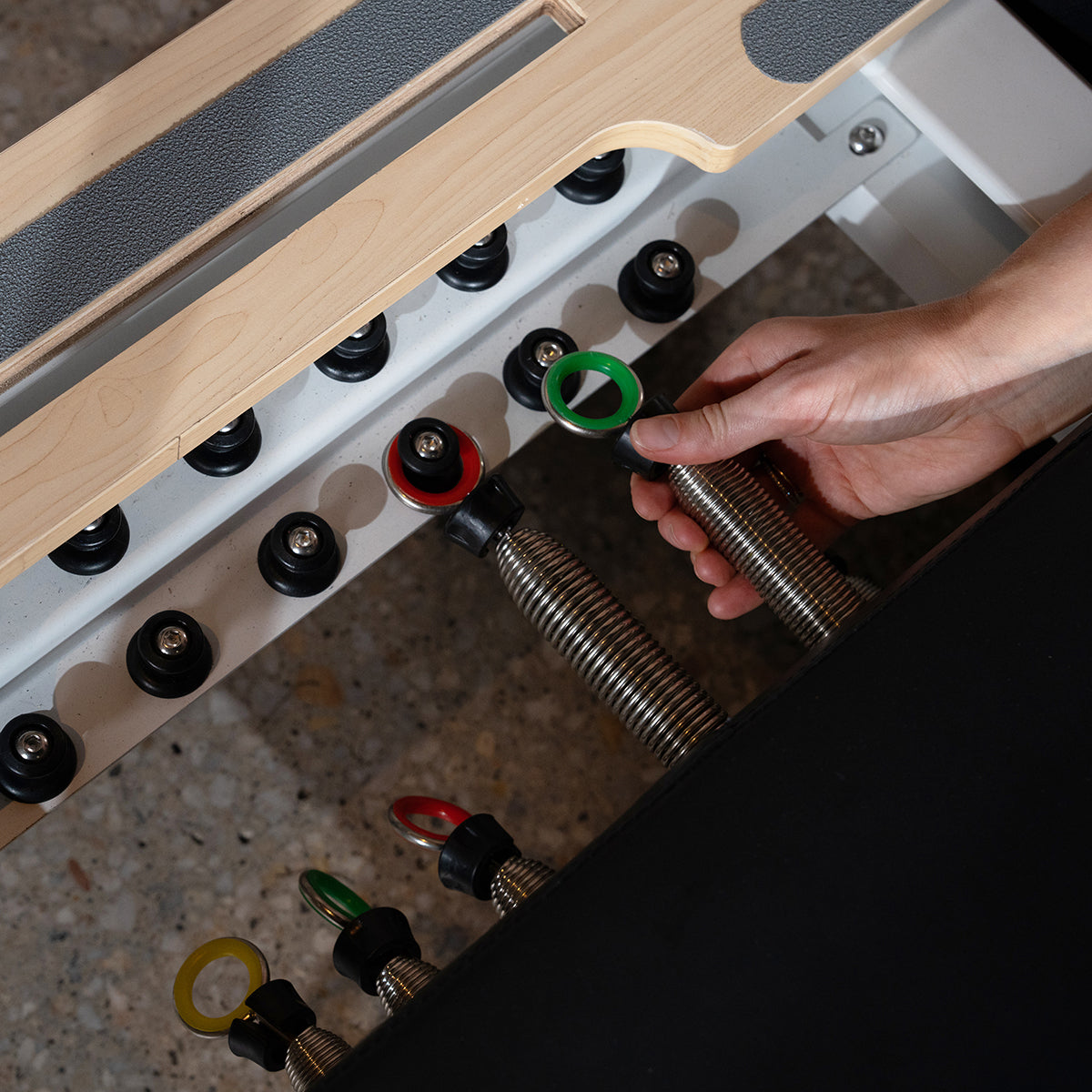 Close-up of a user adjusting resistance springs on the Lifespan Fitness Contour Pro Aluminium Reformer Set, showcasing its versatile spring mechanism for Pilates workouts.