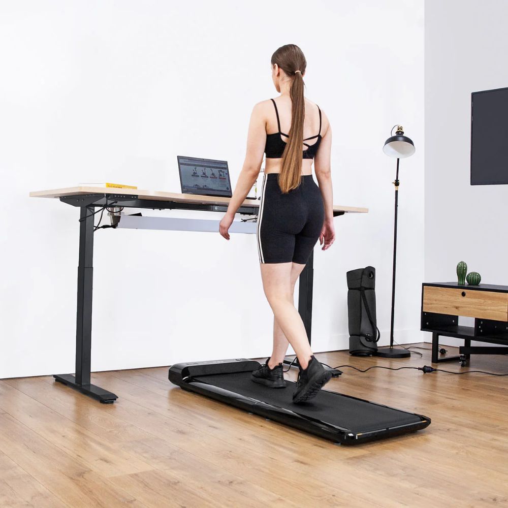 Woman using a walking treadmill under a standing desk for fitness and productivity
