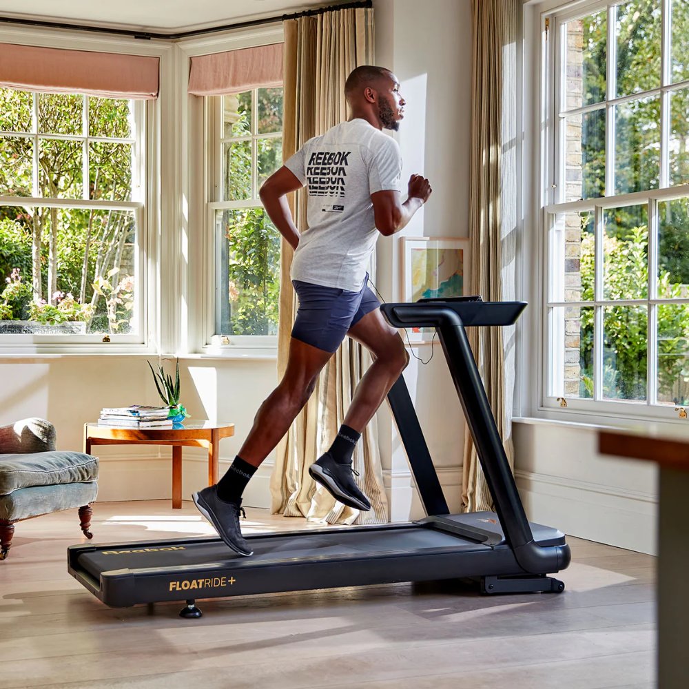 Man running on a treadmill in a bright room with large windows