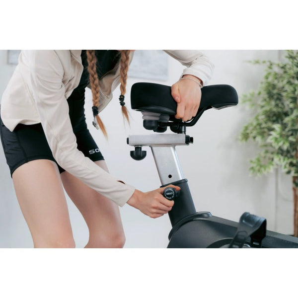 Woman exercising on an indoor stationary bike with a modern console in a bright, stylish room.