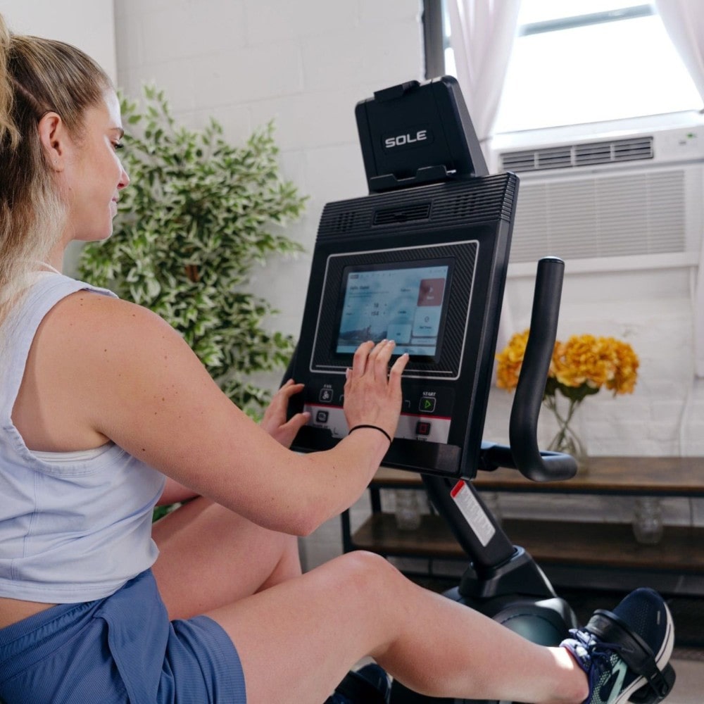 Woman using the Sole LCR recumbent bike for a home workout in a well-lit room