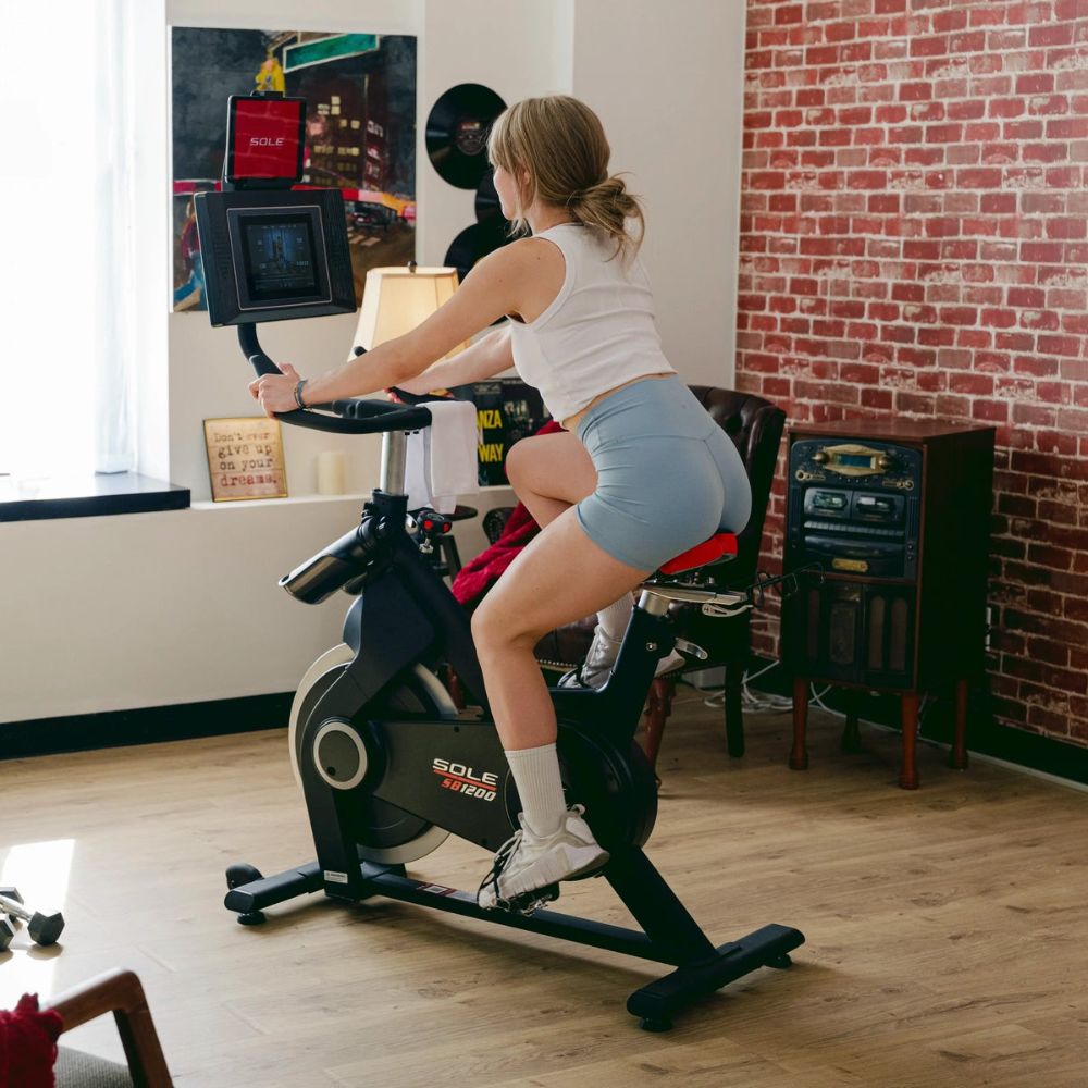 Woman exercising on a Sole 1200 stationary bike in a stylish home gym