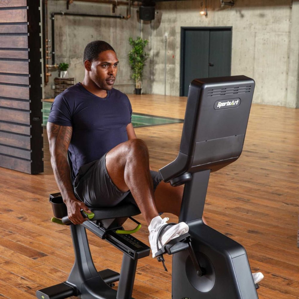 Man using a SportsArt recumbent exercise bike in a modern gym setting